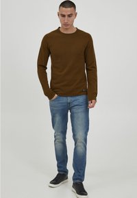 Brown long-sleeve knit shirt with round neckline paired with light wash jeans. Black sneakers complete the casual outfit.