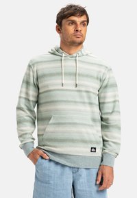 Sudadera de rayas verde claro con bolsillo tipo canguro, cordones, puños acanalados y un parche con el logo en el dobladillo inferior. Tela suave y texturizada.