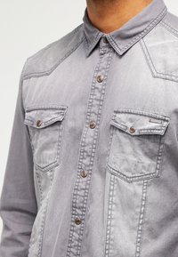 Grijze denim shirt met een button-down kraag, borstzakken, bruine metalen knopen en een vervaagde textuur. Heeft details in westernstijl op de schouders.