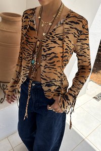 Sheer, brown tiger-striped blouse with a loose fit. Features ties at the cuffs and a deep neckline. Worn over dark high-waisted jeans.