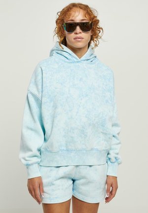 Felpa con cappuccio di colore blu chiaro tie-dye, con un ampio cappuccio e polsini a costine, abbinata a pantaloni corti coordinati. Il tessuto sembra morbido e ha una vestibilità comoda.