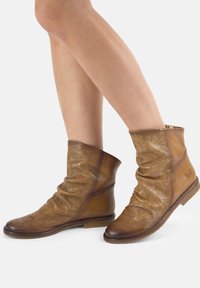 Bottines en cuir marron avec des surfaces texturées, un design décontracté, des motifs perforés et une semelle en caoutchouc plate.