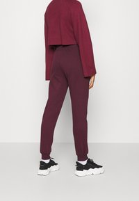 Suéter corto burdeos combinado con pantalones a juego; tejido suave y texturizado; puños ajustados; se lleva con zapatillas negras con suela gruesa.