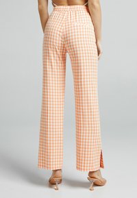 Orange- och vit rutiga byxor med vid ben, elastisk midja och sidoflikar. Materialet verkar vara lätt och ventilerande.