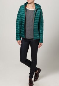 Turkusowa pikowana kurtka z kapturem, poziome przeszycia, zamek błyskawiczny z przodu, połączona z szarym topem i czarnymi wąskimi dżinsami, uzupełniona ciemnymi butami.