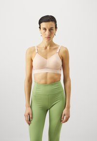 Lys rosa polstret sportsbh med mesh-detaljer og justerbare stropper, kombinert med høyhalsede grønne leggings med en glatt tekstur.