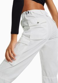 Vita cargobyxor med sidofickor, hög midja med spänne och avslappnad passform. Slät textur med en subtil lyster.