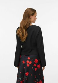 Mustast kangast lühike jakk pikkade varrukatega, millel on sile tekstuur. Modell kannab tumedal taustal punaste roosidega lillemustriga seelikut.