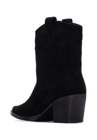 Bota de cowboy de ante negra con un alto tacón cuadrado y costuras decorativas a lo largo del caña, con punta redondeada y detalle de tira para tirar.