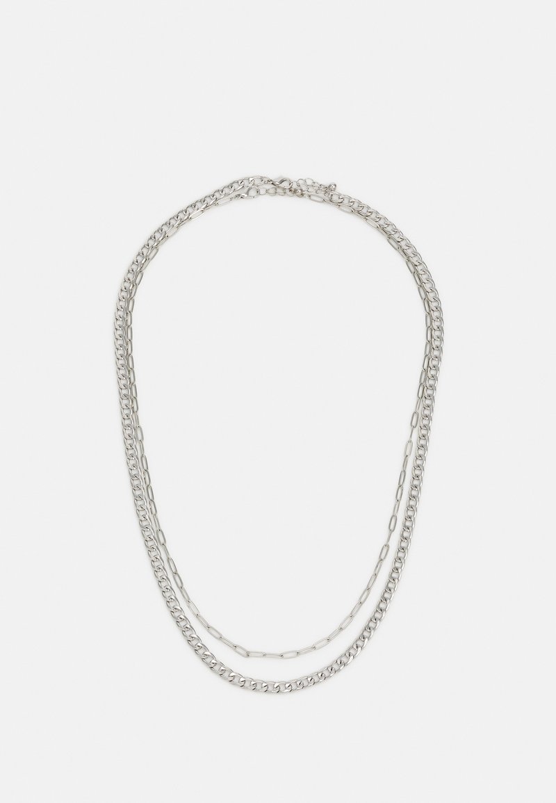 Colar de corrente em camadas de prata, apresentando uma combinação de cadeias com elos ovais e uma corrente com elos redondos, exibindo texturas e espessuras variadas.