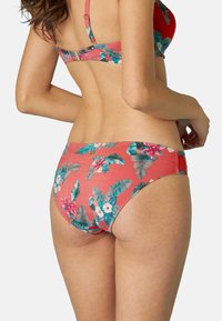 Slip bikini floreale rosso con foglie verdi e fiori bianchi, dal tessuto liscio e con un taglio a vita bassa. Lacci laterali regolabili.