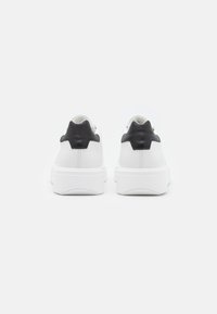 Adidași albi din piele cu accente negre din piele la călcâi, având o talpă groasă albă și un design neted, curat.