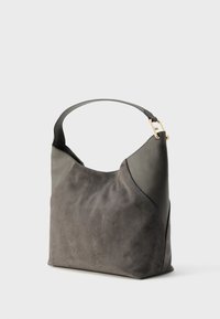 Sac à main en daim gris et cuir avec une bandoulière unique et un détail de boucle dorée sur un fond blanc uni.