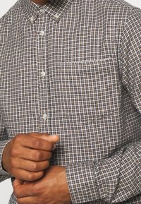 Bruine en witte geruite overhemdd met een zak, met een klassieke kraag en een gestructureerde stof. Korte mouwen zichtbaar.