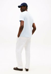 Camiseta de manga corta azul claro, pantalones blancos y zapatos oscuros. Modelo con una gorra azul marino, visto desde atrás. Diseño simple y limpio.