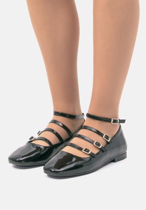 Bailarinas de charol negro con tres correas ajustables en el tobillo que presentan hebillas doradas, diseño de punta afilada y suela plana.