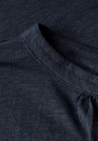 Tmavě námořnické tričko s jemnou texturou, kulatým výstřihem a decentními švy. Materiál má mírné melírování po celé ploše.