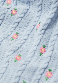 Jasnoniebieska dzianina o fakturowanej powierzchni z białymi warkoczami, haftowanymi różowymi kwiatami z żółtymi środkami oraz zielonymi liśćmi w powtarzającym się wzorze.