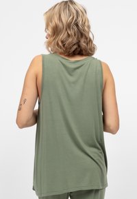 Oliwkowy top bez rękawów o luźnym kroju, wykonany z miękkiego materiału, z okrągłym dekoltem i widocznymi detalami szwów. Brak widocznych wzorów lub akcentów.