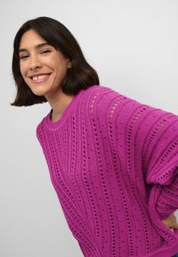 Maglione rosa lavorato a maglia con strisce orizzontali, motivi a trama aperta e una vestibilità rilassata. Il design include polsini e scollo a coste.