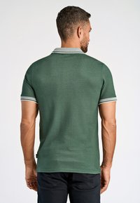 Polo de color verde oscuro con mangas cortas, que presenta un cuello y puños de color gris claro con un patrón de bandas. Fabricado en un tejido de punto texturizado.