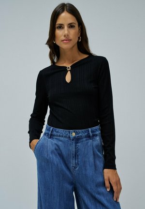 Top negro de canalé de manga larga con escote en forma de lágrima y detalle en tono dorado, combinado con pantalones de mezclilla de talle alto en azul.