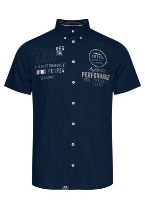 Marineblå kortermet skjorte med knapper, som har broderte detaljer, inkludert tall og tekst, samt en rund kant.