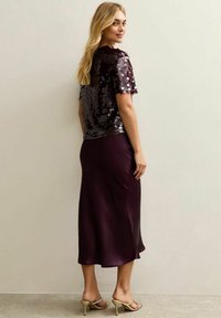 Fioletowa bluzka z cekinami z krótkimi rękawami w połączeniu z satynową spódnicą midi. Gładka faktura, dopasowany krój i minimalistyczny styl.