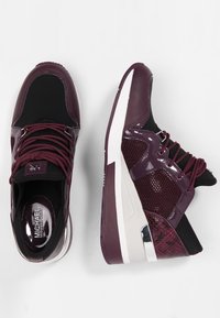 Ett par mörkröda och svarta Michael Kors-sneakers med vita och silverfärgade detaljer, visade från ovan och sidan mot en vit bakgrund.