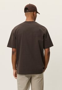 Καφέ φαρδιά μπλούζα από μαλακό βαμβάκι με στρογγυλή λαιμόκοψη. Διαθέτει κοντά μανίκια και άνετη εφαρμογή, συνδυασμένη με ανοιχτό μπεζ παντελόνι.