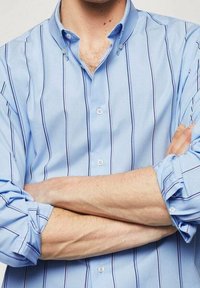 Camisa de botones azul claro con rayas verticales azules oscuras, con cuello y mangas largas, la tela parece suave y ligeramente brillante.