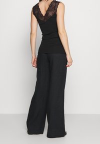 Svart ribbad tanktop med en spets V-ringning och rygg, kombinerad med löst sittande svarta linnbyxor. Har en avslappnad silhuett och texturerade detaljer.