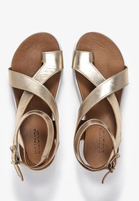 Złote metaliczne sandały z krzyżującymi się paskami, brązową skórzaną wkładką, regulowaną klamrą i białą gumową podeszwą. Gładka faktura.