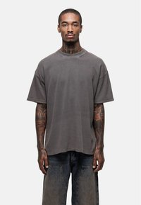 Grijze oversized T-shirt met een geribde textuur, korte mouwen en een ronde halslijn. Draagt met relaxte, donkere spijkerbroek.