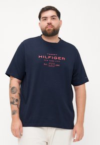Granatowa bawełniana koszulka z krótkim rękawem, z czerwonym logiem i brandingiem "Tommy Hilfiger". Luźny krój z okrągłym dekoltem.