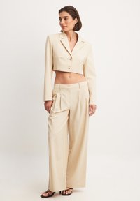 Beige cropped blazer met twee knopen, gecombineerd met wijde broek. Glad textuur, op maat gemaakt pasvorm en minimalistisch ontwerp. Zwarte sandalen.