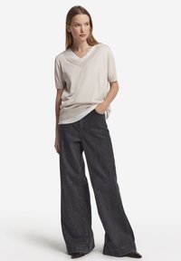 Beige stickad V-ringad topp med korta ärmar, kombinerad med vida mörkgråa denimbyxor. Mjuk textur med avslappnad passform.