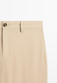 Beige chinos made of cotton, featuring a button closure, belt loops, and a smooth texture. Includes side pockets and a classic design.