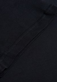 Svart tyg med en slät textur, som har ett subtilt ribbat mönster. Sömmarna syns längs kanterna, vilket framhäver plagget konstruktion.