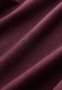 Vínová látka s texturovaným tkaným vzorem; měkký vzhled s zvlňujícími se záhyby, představující hlubokou, bohatou barvu.