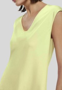 Canottiera gialla senza maniche con scollatura a V, realizzata in tessuto liscio, caratterizzata da una vestibilità comoda e da una leggera lucentezza.