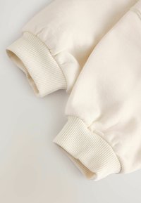 Cremfarbene Baumwoll-Sweatshirtbündchen mit geripptem Textur und einem gerafften, puffigen Design. Weicher Stoff mit glatter Oberfläche.