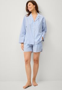 Lichtblauw en wit gestreept pyjama set bestaande uit een overhemd met lange mouwen en bijpassende shorts. Gemaakt van katoen met een zak.