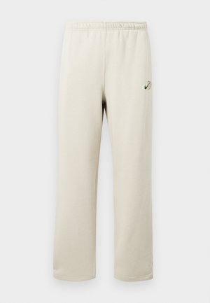 Μπεζ φόρμες με ελαστική μέση, ίσια πόδια και μικρό πράσινο και μαύρο λογότυπο Nike στο πάνω αριστερό μηρό.