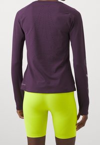 Długi rękaw purpurowy top sportowy z perforowanym wzorem z tyłu, w zestawie z dopasowanymi neonowo-żółtymi szortami. Gładki materiał, sportowy krój.