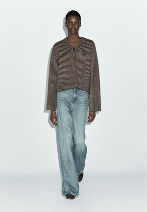 Cardigan a righe marroni con scollo a V e jeans azzurri a vestibilità morbida. Le texture sono morbide, con una silhouette rilassata e un design semplice.