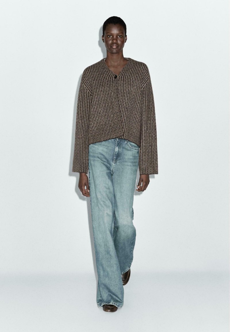 Bruine gestreepte cardigan met een V-hals en losse, lichtblauwe jeans. De texturen zijn zacht, met een ontspannen silhouet en eenvoudig ontwerp.
