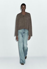 Brązowy prążkowany sweter na guziki z dekoltem w serek, zestawiony z jasnoniebieskimi szerokimi spodniami i brązowymi butami. Prosty i luźny krój.