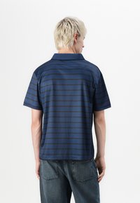 Marineblå polo skjorte med horisontale mørkeblå striper, korte ermer og krage. Stoffet virker glatt med en vanlig passform.