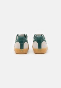 White and green sneakers with a suede and leather finish, featuring a gum rubber sole and embossed "GUESS" logo on the heel.
